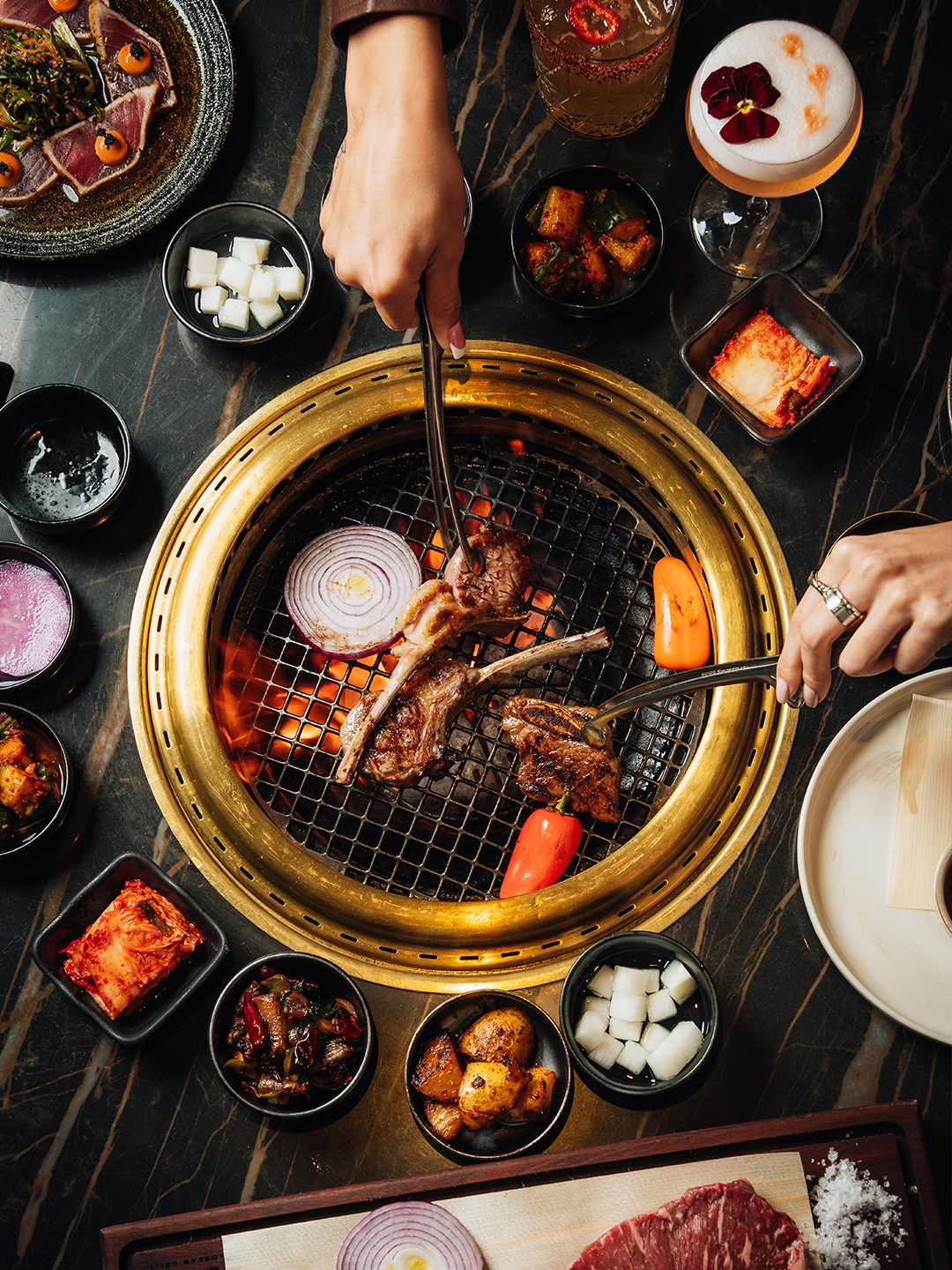 overhead view of korean bbq grill with someones hands cooking and food on table